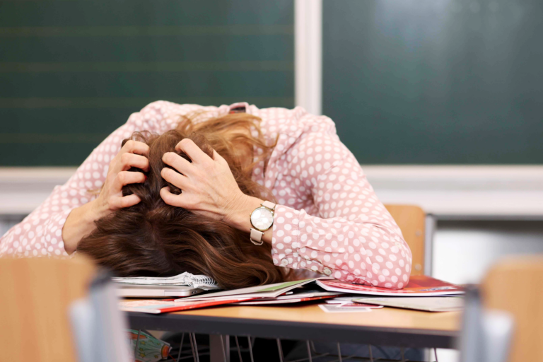 Stressfrei unterrichten Onlinekurs von Meike Haas, Meike Haas sitzt in einem Klassenzimmer am Lehrerpult und rauft sich verzweifelt die Haare