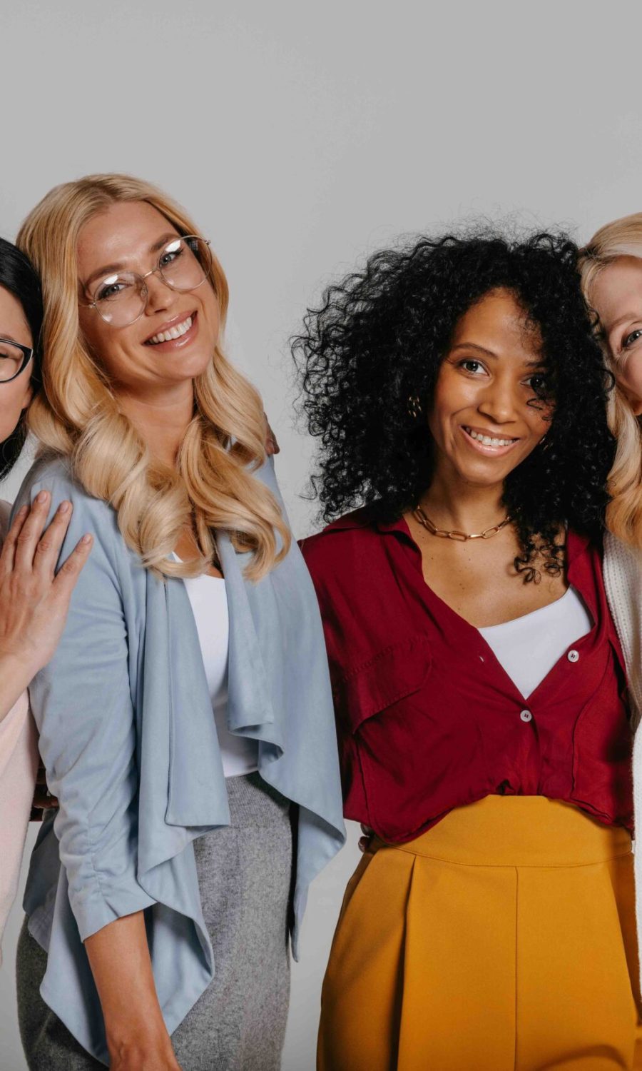 Multi-ethnic group of beautiful mature women bonding and smiling against grey background